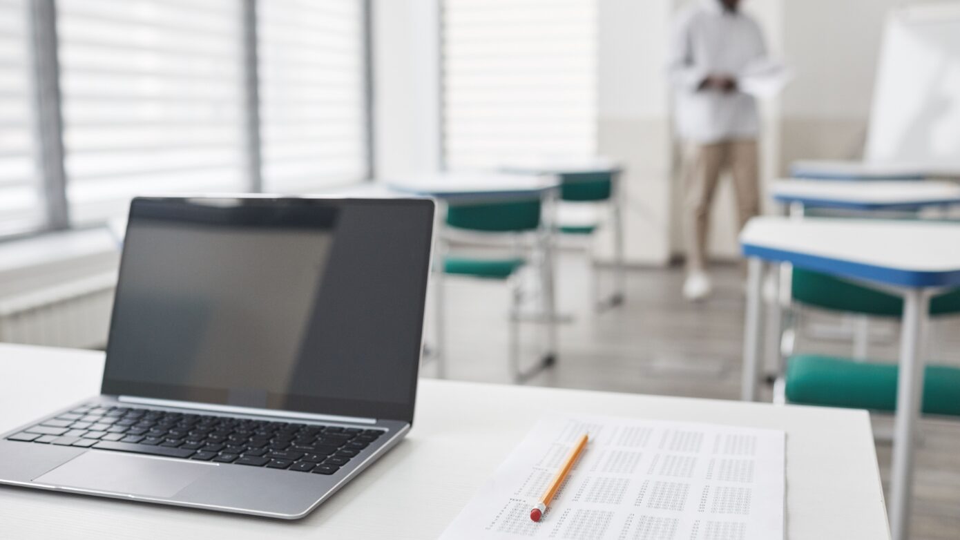 Laptop and exam sheet on a desk in a modern classroom setting.