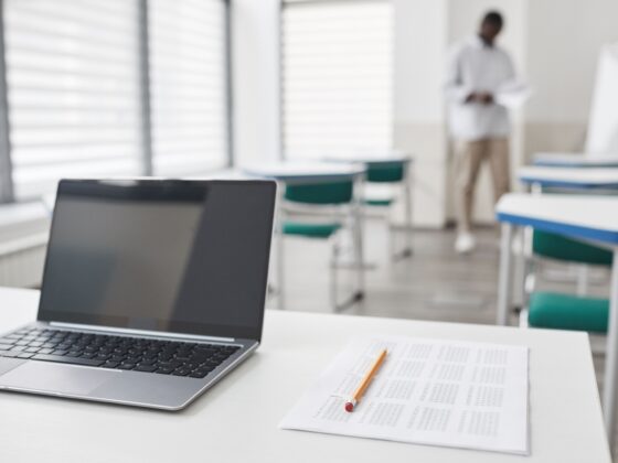 Laptop and exam sheet on a desk in a modern classroom setting.