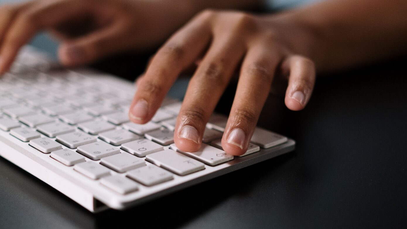 A close-up view of hands typing on a sleek white wireless keyboard on a desk.