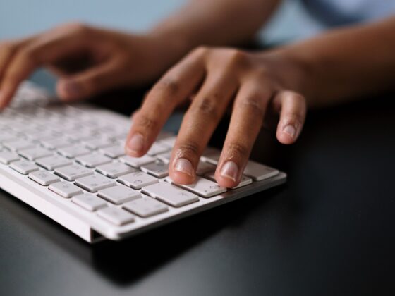 A close-up view of hands typing on a sleek white wireless keyboard on a desk.