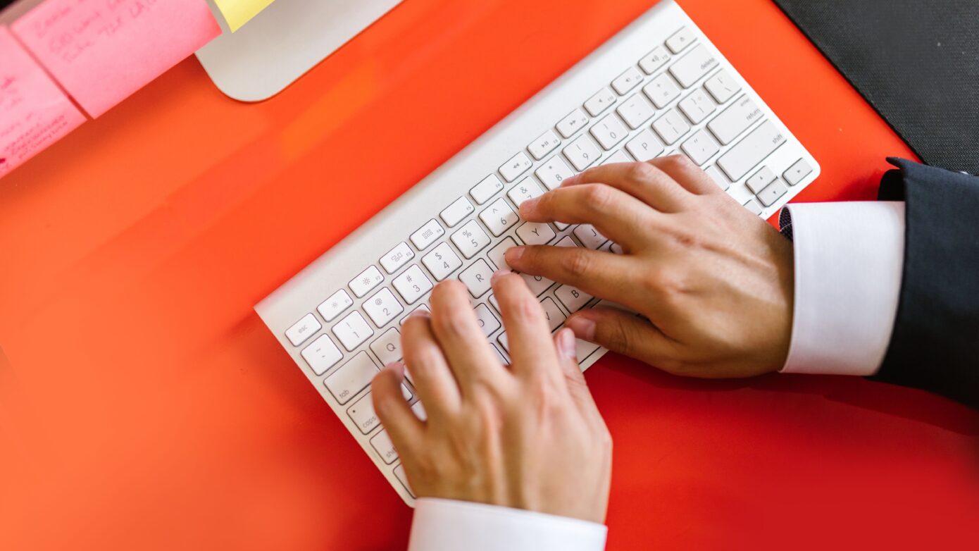 Close-up of hands typing on a wireless keyboard on an orange desk, ideal for tech and business themes.