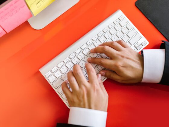 Close-up of hands typing on a wireless keyboard on an orange desk, ideal for tech and business themes.